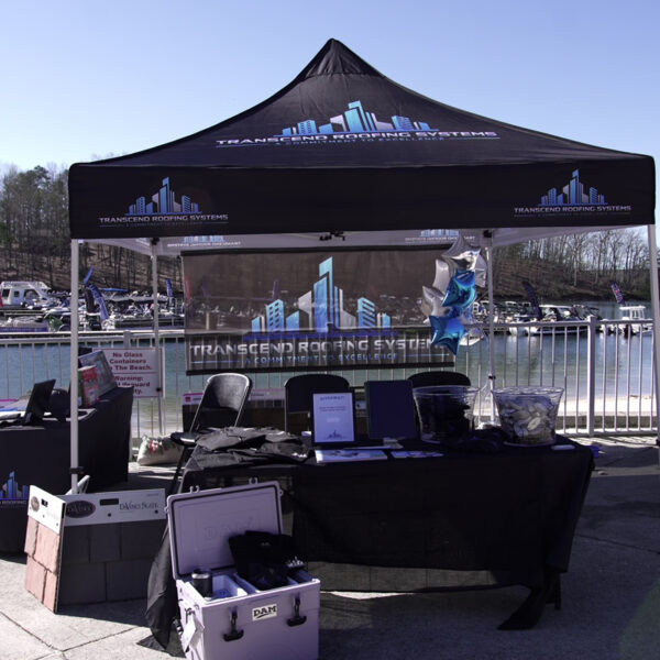 A Transcend Roofing Company tent is set up near a lake.