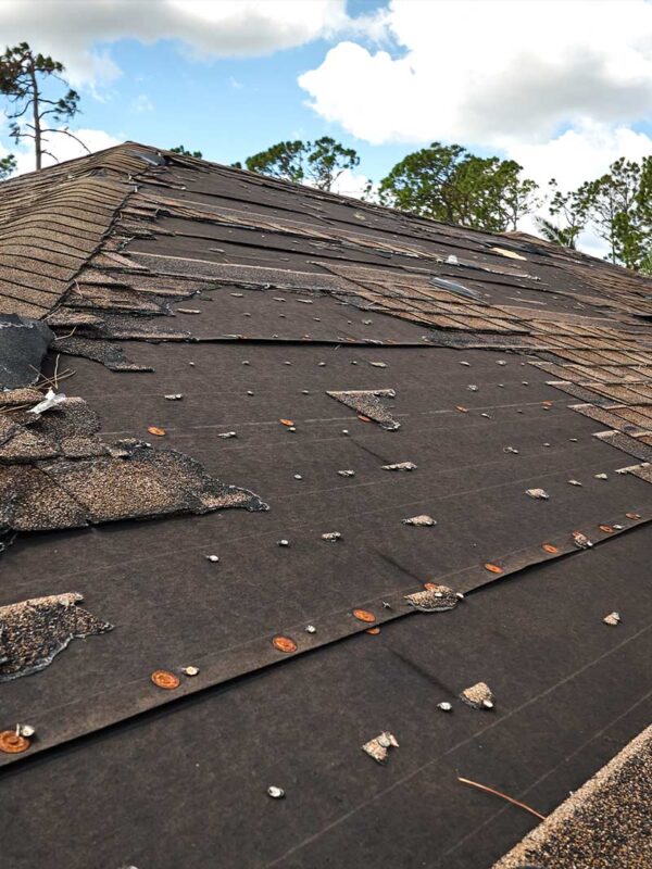 The roof, with missing and damaged shingles exposing underlying materials, sits quietly under a partly cloudy sky. With its expertise, Transcend Roofing Systems could bring it back to excellence.