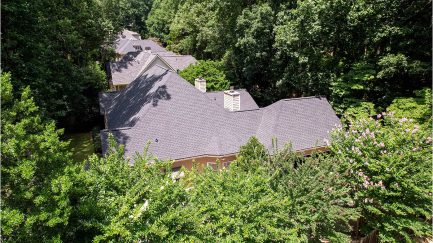 Aerial view of several houses with gray roofs surrounded by dense green trees and foliage.