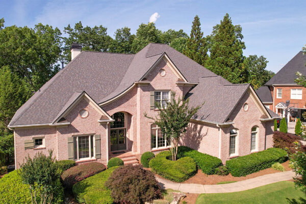 Two-story brick house with multiple gables, large front windows, manicured bushes, and a curving sidewalk, surrounded by trees on a sunny day. Two-story brick house with multiple gables, large front windows, manicured bushes, and a curving sidewalk, surrounded by trees on a sunny day.