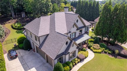 Aerial view of a two-story suburban house with a well-maintained yard, surrounding trees, a driveway, and a parked car.