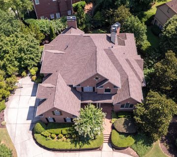 Aerial view of a large two story brick house with a complex roof, surrounded by trees, lawn, and a curved driveway 