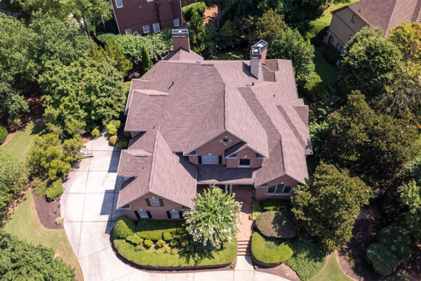 Aerial view of a large two-story brick house with a complex roof, surrounded by trees, lawn, and a curved driveway. Aerial view of a large two-story brick house with a complex roof, surrounded by trees, lawn, and a curved driveway.